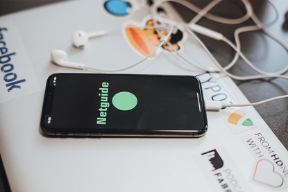 Smartphone mit Schriftzg "Netguide" auf dem Display liegt auf einem Laptop.